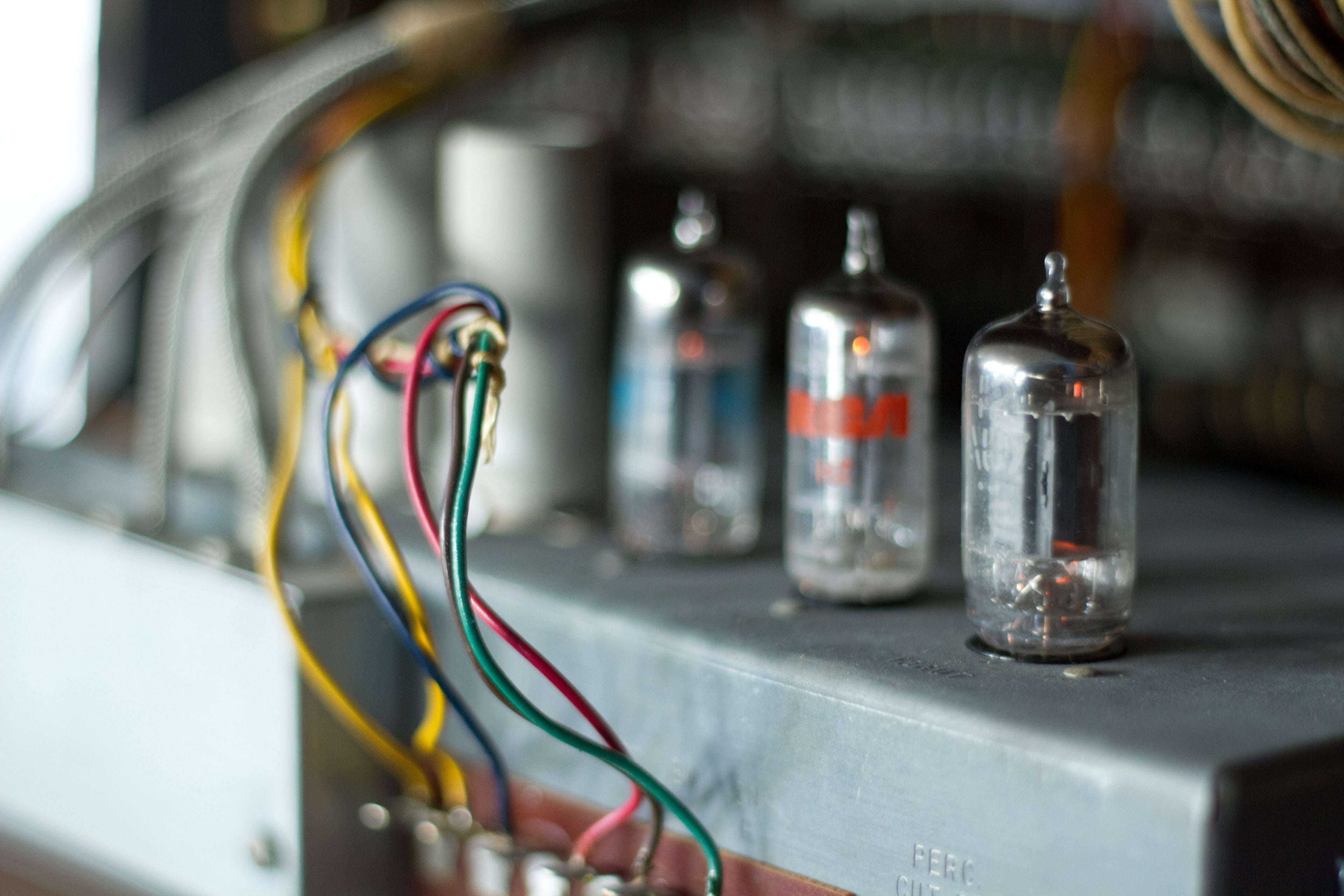 Close-up of three glass vacuum tubes mounted on a gray metal chassis inside a 1956 Hammond B3 organ.